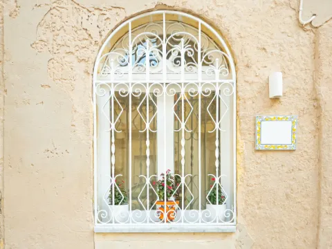 Grille de fenêtre cintrée en fer forgé blanc sur un mur d'enduit ocre clair