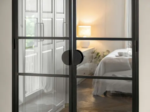 Porte verrière à deux battants et cadre d'acier noir ouvrant sur une chambre lumineuse